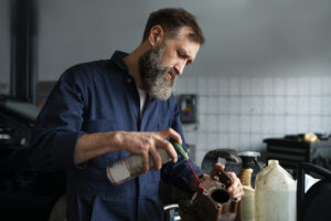 Mecânico aplicando lubrificante em peça de carro em oficina, destacando a importância da lubrificação adequada para prevenir falhas nos rolamentos e garantir a eficiência dos componentes automotivos.