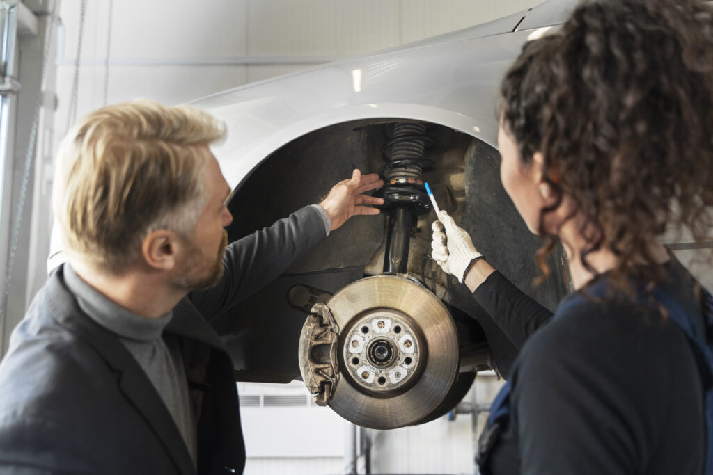 Profissionais avaliando componentes da roda e da suspensão de um carro, ilustrando sinais de junta homocinética automotiva ruim, desgaste no sistema de transmissão e necessidade de manutenção.