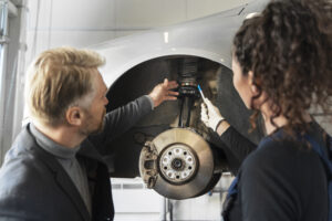 Profissionais avaliando componentes da roda e da suspensão de um carro, ilustrando sinais de junta homocinética automotiva ruim, desgaste no sistema de transmissão e necessidade de manutenção.